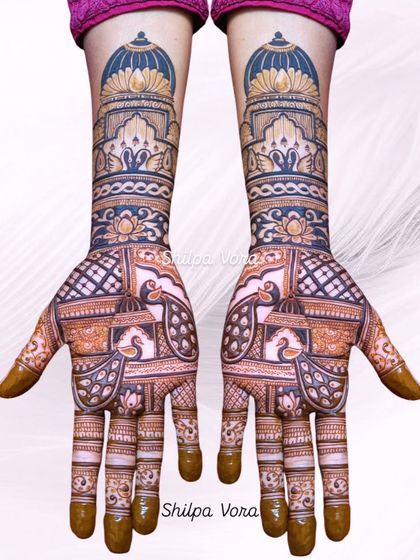 A grand bridal design with architectural jharokha elements at the wrist and peacock figures in the palm. The dark and light shading creates a 3D effect.