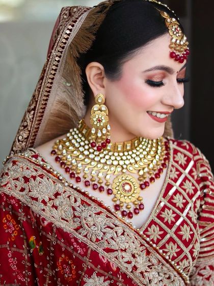 A close-up of the bride's makeup, showing the soft copper eyeshadow and perfectly matched lip color that complements her red and gold jewelry.
