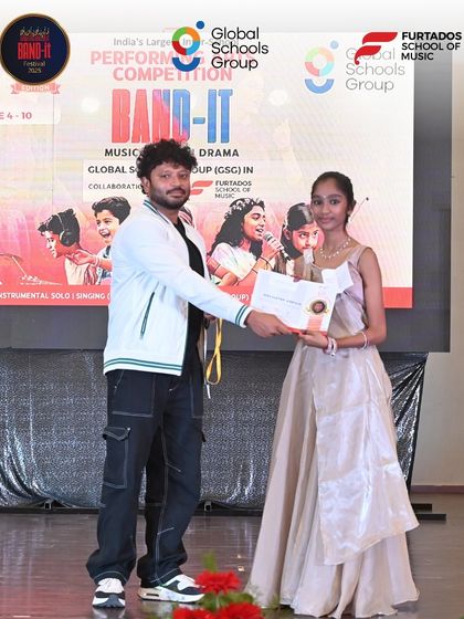 A young vocalist receives her award on stage at the Bangalore Band-It event. Her elegant attire and proud smile capture the culmination of her hard work and successful performance.