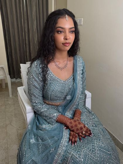 A full-length shot of Sushmita seated, showcasing her elegant blue lehenga. The makeup and hair are styled to create a cohesive and modern bridal look.