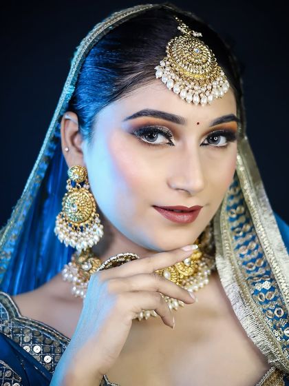 A Muslim bridal look in a royal blue outfit, featuring a smokey eye and heavy gold jewelry.