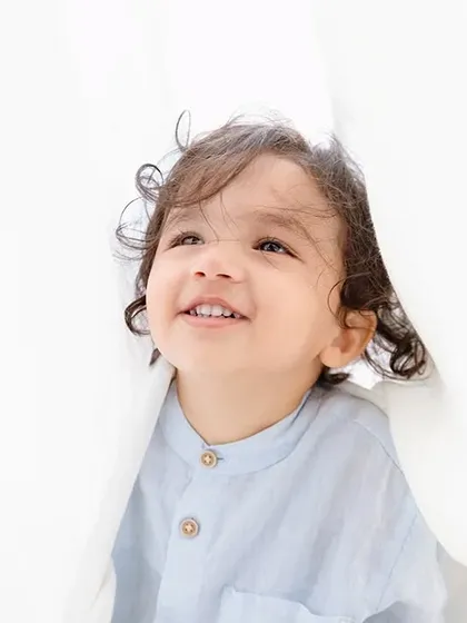 A playful toddler peeks through white curtains. I love finding creative ways to capture the curious and fun-loving nature of toddlers.