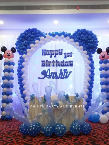 A Mickey Mouse themed first birthday stage in blue and white. The centerpiece is a large Mickey-ear-shaped balloon arch framing the backdrop.