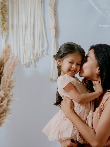 A beautiful, candid moment where the mother is kissing her smiling daughter's cheek. The genuine emotion in this shot makes it a priceless memory.
