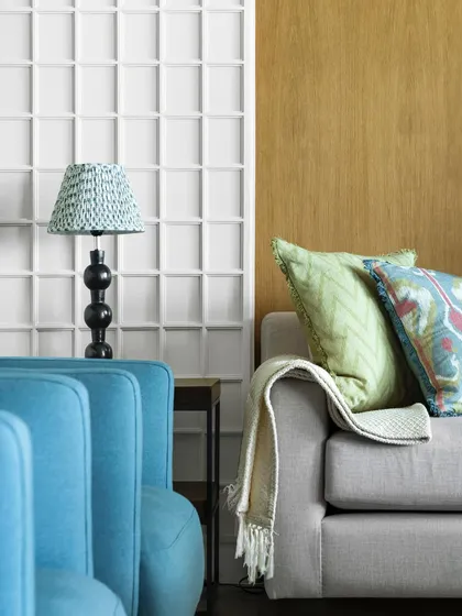 Another view of the living room, highlighting the play of colors and textures. The bright blue armchairs provide a striking contrast to the warm wood paneling and neutral sofa.