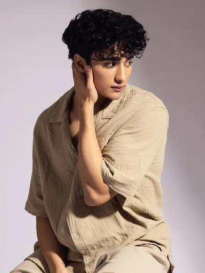 A soft, warm-lit portrait. The makeup is natural and enhances his features without being obvious.