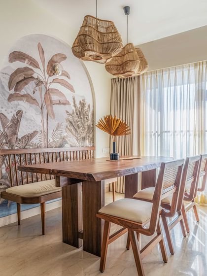 A closer look at the dining nook, where rattan pendant lights hang above a solid wood table. The custom wallpaper, featuring muted tropical palms, adds depth and artistry to the space, enhancing the home's connection to nature.