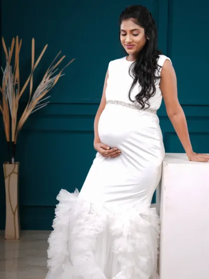 A vision in white. This fitted mermaid gown with a ruffled train is the epitome of elegance and sophistication for a maternity shoot.