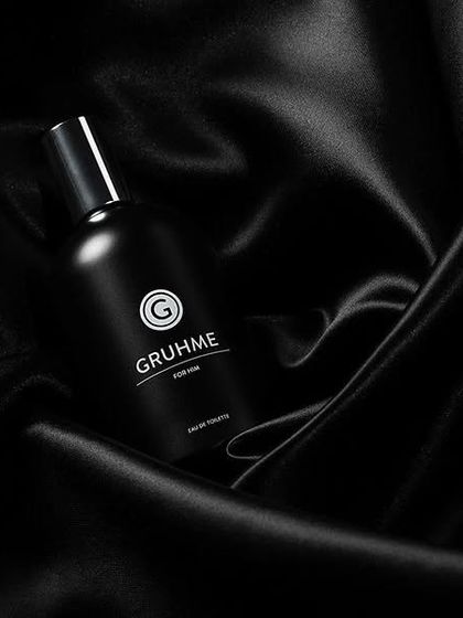 A bottle of Gruhme men's perfume nestled in black silk. The soft, flowing fabric contrasts with the matte black bottle, creating a sense of luxury and elegance.