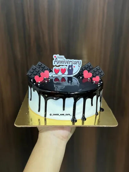 A delicious-looking chocolate drip anniversary cake, topped with chocolate bars and hearts.