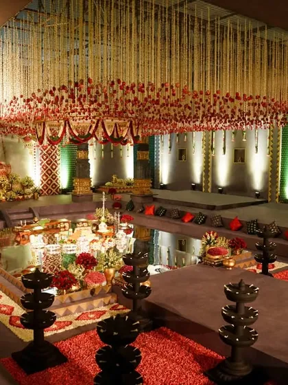 An overview of the main wedding hall, showing the central mandap, the surrounding water body, and the tiered guest seating. The ceiling is a canopy of thousands of suspended tuberose and red rose strings, creating a breathtaking floral spectacle.