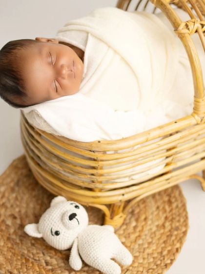 A classic newborn pose, sleeping peacefully in a rustic wicker basket. The simple setup keeps the focus on the baby's natural beauty.