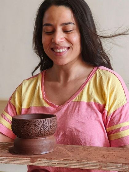 A participant smiles, delighted with the leaf-textured bowl she has just created. Our workshops focus on both wheel throwing and hand-building decoration techniques like texturing.