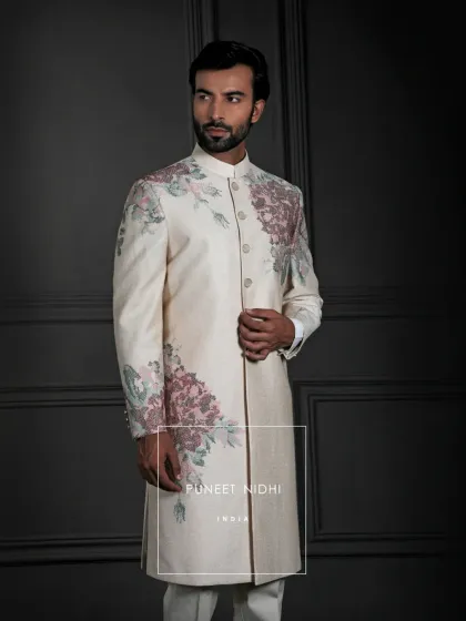 An ivory silk Achkan where artistry blooms. The clean, straight cut is a canvas for blush-pink and sage-green floral embroidery that sweeps across the shoulders and cuffs, a testament to modern elegance and timeless craftsmanship.