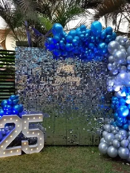 An outdoor 25th birthday party with a blue and silver theme. This setup includes a large sequin wall, a balloon garland, and marquee numbers.
