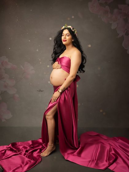 A confident and striking solo portrait. The mother-to-be stands tall in a magenta fabric wrap gown, her pose exuding strength and beauty.