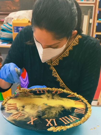 A student carefully adding gold leaf details to the border of her resin clock, a technique we teach for adding a touch of luxury to your artwork.