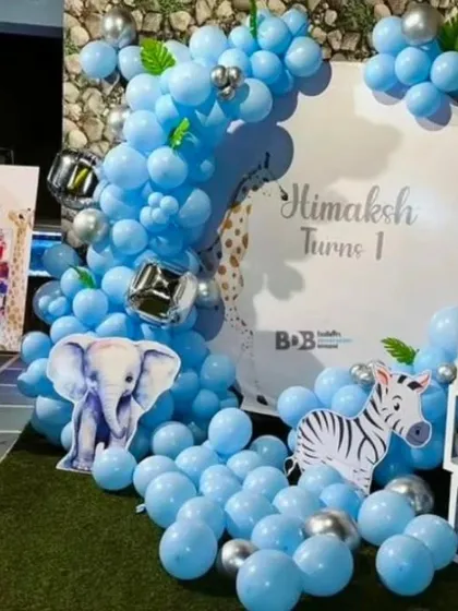 A cute blue-themed jungle or safari party for a first birthday. The decor includes elephant and zebra cutouts, 'BABY' blocks, and a personalized photo collage.