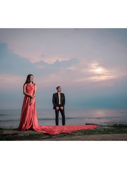 A serene pre-wedding photo at the beach as the sun sets. The bride's long pink gown trails behind her, creating a beautiful contrast with the calm sea.