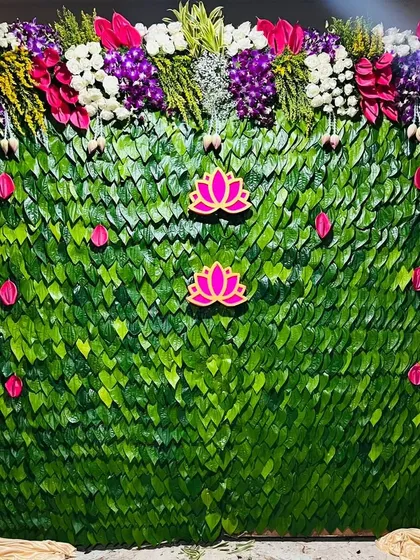 This is a unique backdrop I created using a wall of fresh green leaves. I decorated it with pink lotus cutouts and vibrant flower garlands on the sides, offering a natural and traditional look for any ceremony.