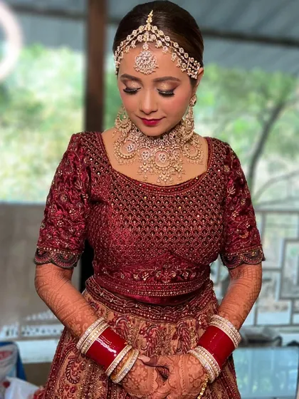 A classic Punjabi bride exuding grace. Her look features a bold lip, shimmering eyes, and a traditional matha patti that frames her face beautifully.