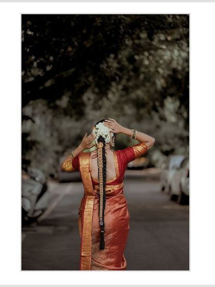 A beautiful shot of the bride from the back, showing off her traditional braid and saree as she walks down a tree-lined street.
