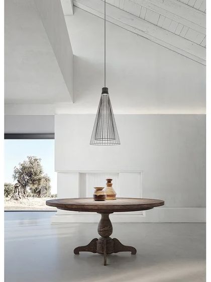 A single Ikonika pendant provides a minimalist focal point over a rustic wooden table in a bright, airy room.