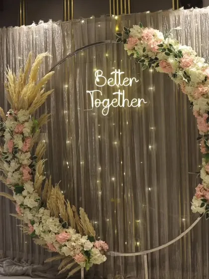 A chic and modern circular backdrop for an engagement or reception. The arch is decorated with pastel flowers and pampas grass, with a "Better Together" neon sign for a personal touch.