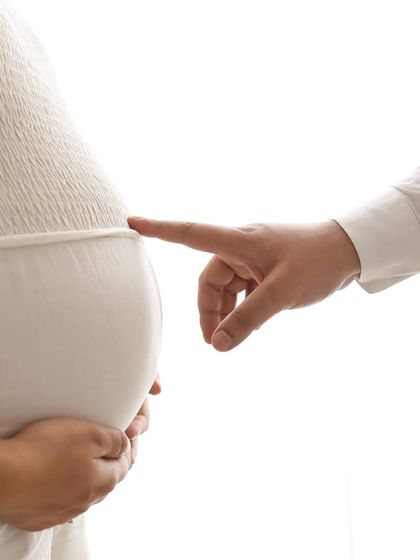 A playful and sweet close-up. The partner's finger gently touches the baby bump, a simple and tiny gesture that is full of meaning and love.
