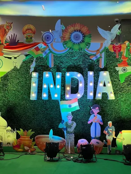 I create large-scale patriotic decor for corporate offices and community events. This Republic Day stage features a massive "INDIA" marquee sign against a green backdrop, surrounded by cutouts representing our country's diverse culture and achievements.