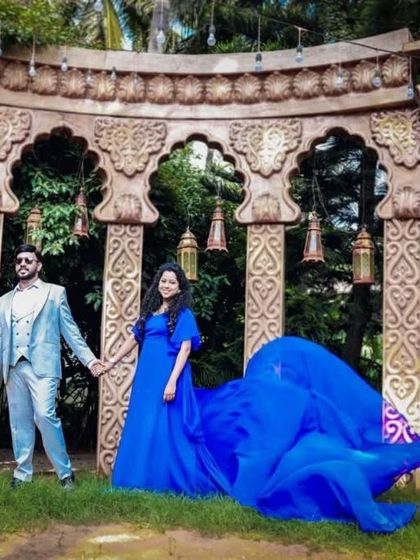 A beautiful pre-wedding photo in a grand architectural setting. The couple looks regal in a blue flying gown and a light grey three-piece suit.