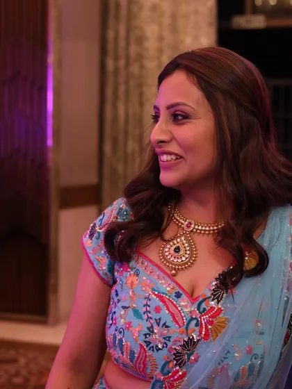 A candid shot showing the beautiful details of the custom-embroidered blouse and the elegant gold necklace. The soft, loose hairstyle complements the entire look.