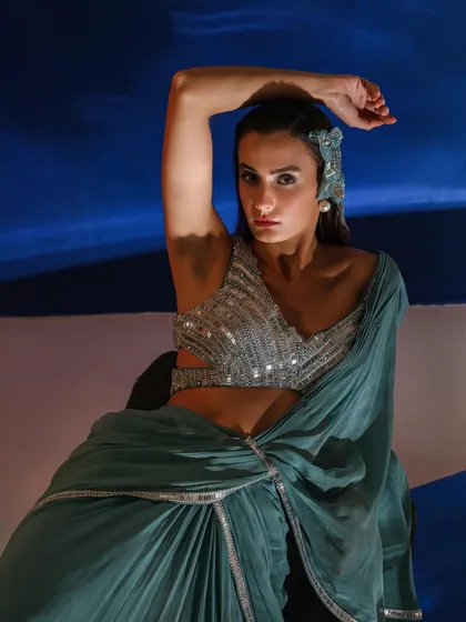 A modern take on ethnic wear, featuring a pre-draped saree with a heavily embellished blouse. The styling is enhanced by a statement headpiece, adding a touch of avant-garde elegance.