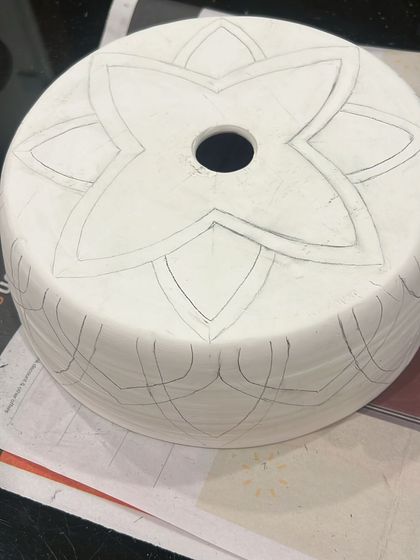 The journey of a lampshade begins with a pencil sketch on greenware (unfired clay). This is where the design is carefully planned before any carving or color is added.