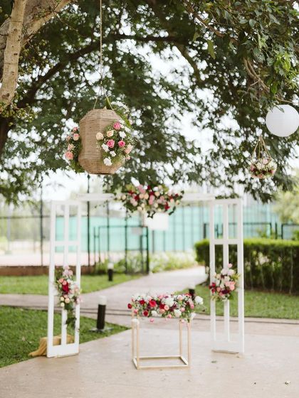 This photo shows a simple and elegant outdoor setup for guests. We used clean white frames decorated with pink and red flowers, along with hanging floral baskets to define the space beautifully.
