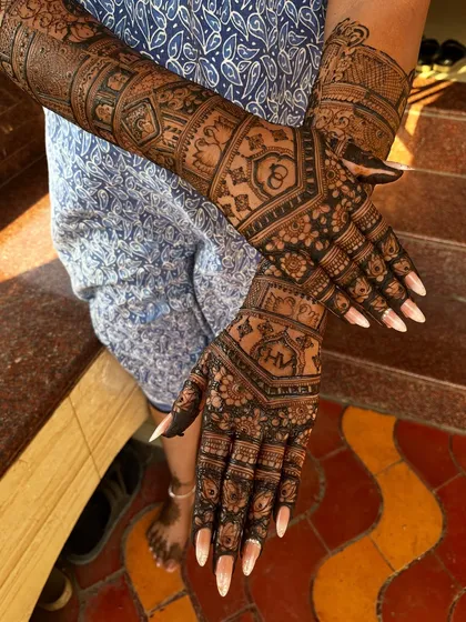 The back-hand view of a heavy engagement mehendi. The design features interlocking geometric patterns and the couple's initials, 'H' and 'V', hidden within a creative motif.
