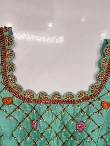 The front neckline of the mint green blouse, showcasing the delicate scalloped border and the continuation of the embroidered lattice pattern.
