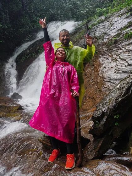 A couple in bright ponchos posing happily at a waterfall on the Kodachadri trail.