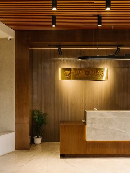 The reception desk at the Vision office combines warm wood paneling with a sleek marble front, creating a professional and welcoming first impression. The backlit logo adds a touch of sophistication.