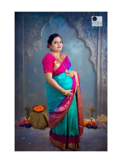 A full-length portrait from the same traditional maternity session. This pose beautifully showcases both the baby bump and the graceful drape of the saree, surrounded by festive elements like diyas and flowers.