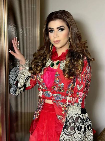 A client ready for a party in a stunning red embroidered outfit. Her hair is styled in large, bouncy curls, creating a look that is both festive and glamorous.