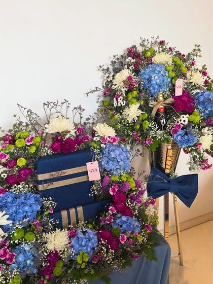 A sophisticated and grand display in shades of royal blue and purple. This setup includes a large floral arrangement for gifts and a matching bouquet with a bottle of champagne.