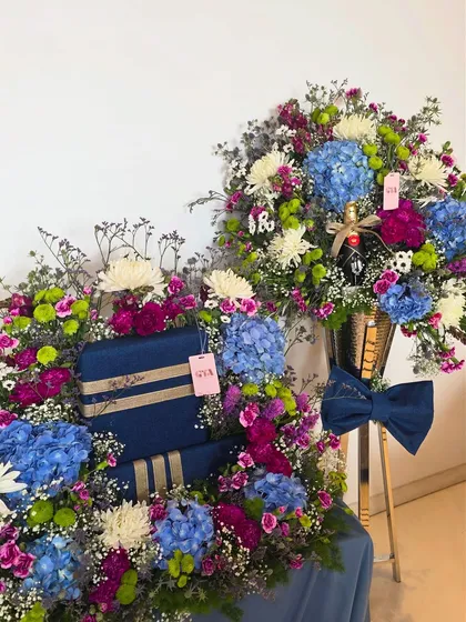 This image shows the complete gift set, with a large floral arrangement on a stand and a coordinating gift tray filled with beautifully wrapped boxes and matching flowers.