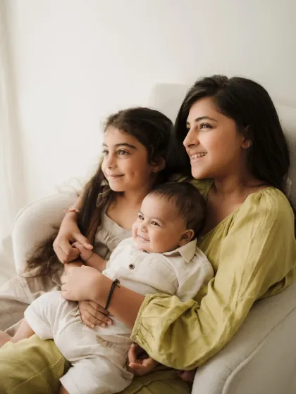 Three siblings sit together on a white armchair, sharing a happy moment. This photo showcases the beautiful bond between them.