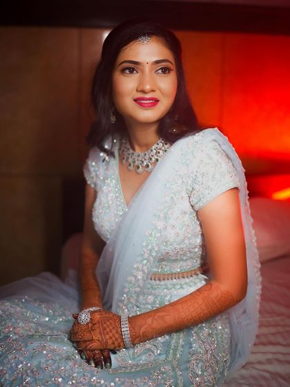 Rakshita seated, looking elegant and poised. The red lighting adds a dramatic flair to her cool-toned outfit and makeup.