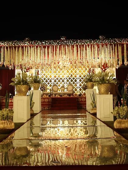 A mirrored aisle reflects the opulent decor, leading to a mandap adorned with traditional floral hangings and gold accents. This design creates a grand sense of arrival for the ceremony.