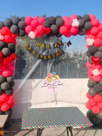 An outdoor anniversary decoration with a black and red balloon arch.