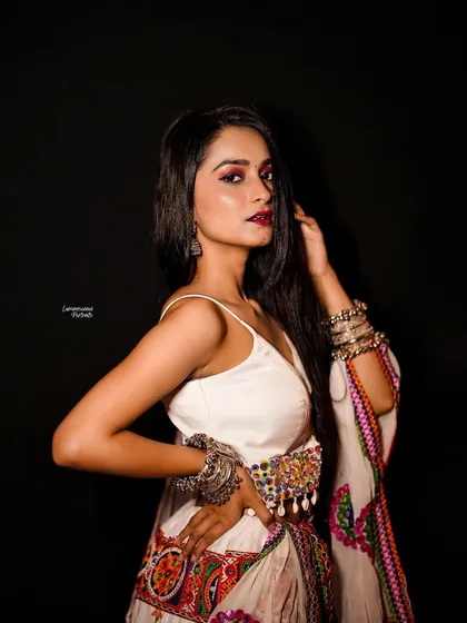 A bold and confident pose in a Navratri-themed studio shoot, showcasing the detailed craftsmanship of the white lehenga and the model's powerful presence.