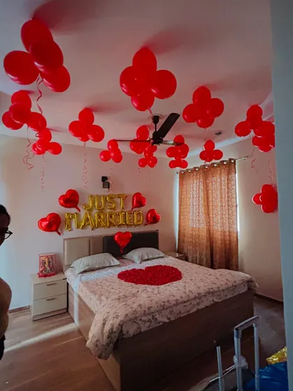 A 'Just Married' decoration for a couple's first night. The room is filled with red balloons and a heart of rose petals on the bed.