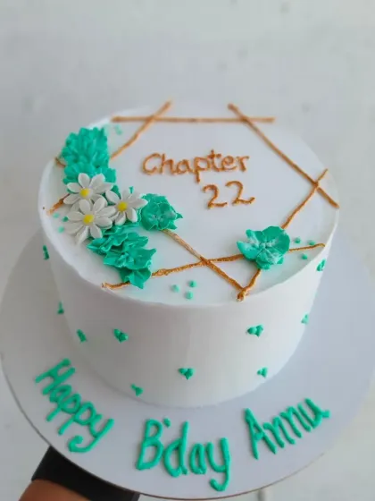 A minimalist birthday cake with a geometric gold design and teal floral accents.